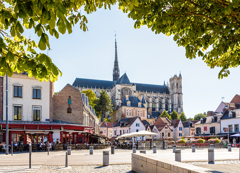 Amiens, France - August 13, 2022: General view of Notre-Dame d'Amiens cathedral overlooking the Don square lined with historic townhouses, sidewalk cafes and restaurants on a sunny summer day.