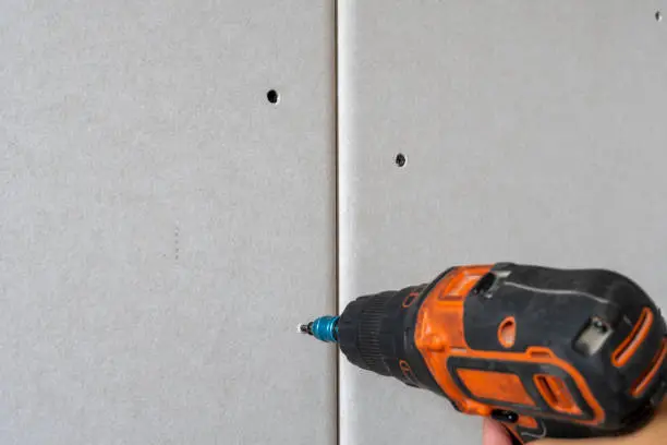 Room repair. Building. Worker fastens drywall with a screwdriver close up
