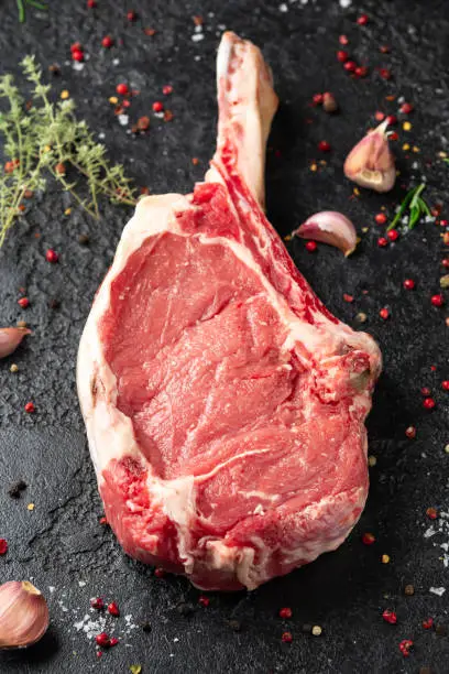 Tomahawk steak on dark stone background with herbs and spices