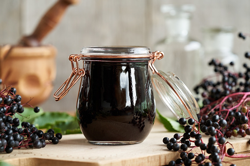 A jar of homemade black elder syrup with fresh elderberries on a wooden table