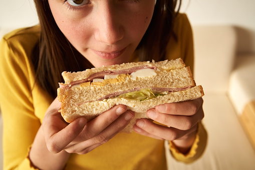 Sandwich with ham, eggs and lettuce held by a teenage girl