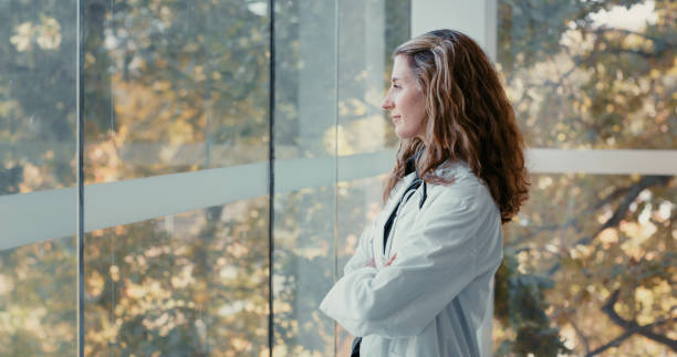 Relax, thinking and happy work mindset looking out a window at nature with a young doctor. Calm, content and serene woman medical and healthcare professional feeling job hope and career happiness stock photo