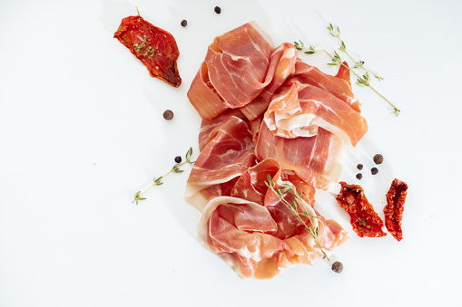 Slices of dried spanish ham with Italian sun-dried tomatoes. Jamon Serrano on the white background. Flat lay