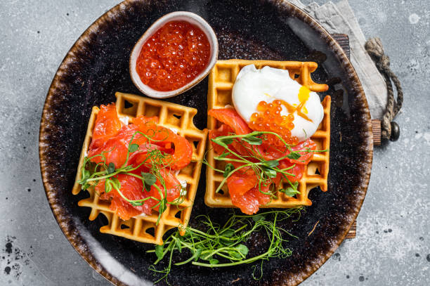 istock Belgian waffle with cream cheese, salmon slices, egg and red caviar. Gray background. Top view 1420715321