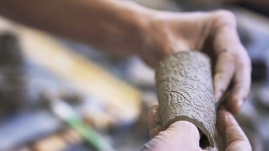 Raw clay with beautiful cut floral ornament. Close up of male hands making decorative dish from raw clay in a workshop, ceramics works concept.