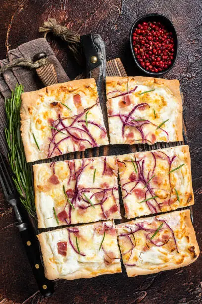 Photo of French tarte flambee with cream cheese, bacon and onions. Flammkuchen from Alsace region.  Dark background. Top view