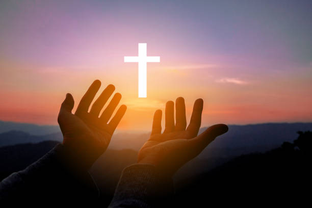 Silhouette of human hands palm up praying and worship of cross, eucharist therapy bless god helping, belief, forgiveness, freedom, hope and faith, christian religion concept on sunset background. stock photo