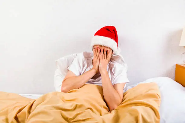 Sad Young Man in Santa Hat in the Bed hide a Face