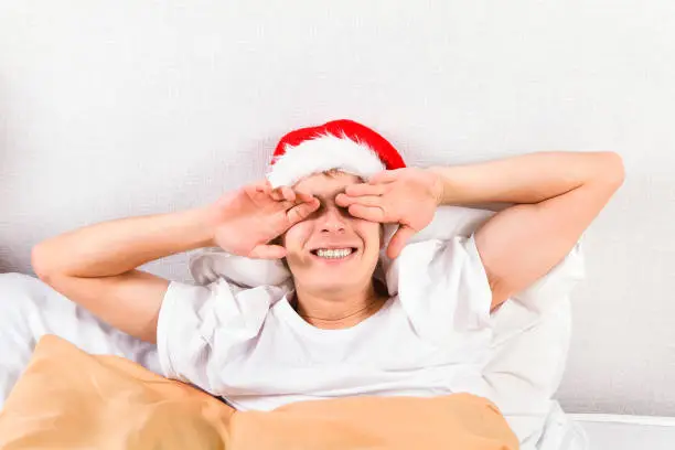 Young Man in Santa Hat cover the Eyes in the Bed at the Home