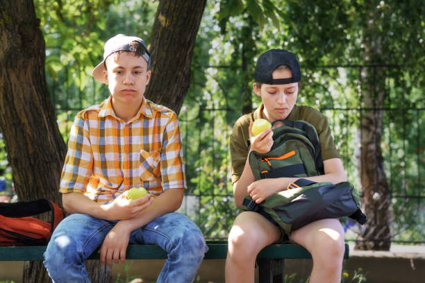 ritratto di studenti in un parco cittadino, scolari adolescenti un ragazzo e una ragazza seduti su una panchina, che riposano e mangiano mele - bench sitting tree apple foto e immagini stock