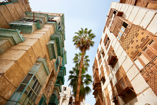 Low angle view of residential buildings featuring vernacular architecture, balconies, and mashrabiya woodwork in historic district of Jeddah, Saudi Arabia.