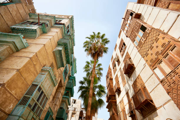 Traditional residential buildings and palm trees in Al-Balad Low angle view of residential buildings featuring vernacular architecture, balconies, and mashrabiya woodwork in historic district of Jeddah, Saudi Arabia. jeddah stock pictures, royalty-free photos & images