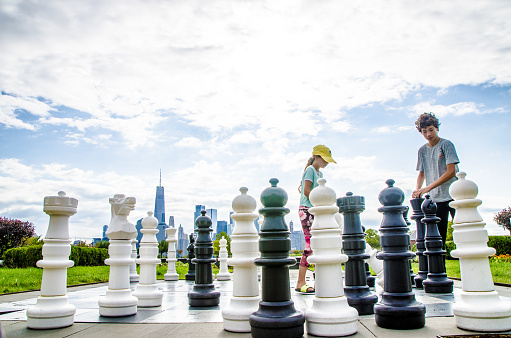 Two teenagers playing chess outside on a giant chess set in Liberty state park with New York city in background
