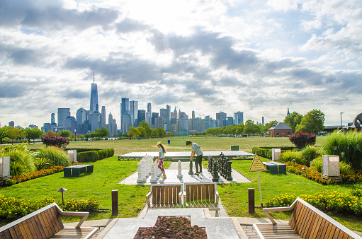 Two teenagers playing chess outside on a giant chess set in Liberty state park with New York city in background