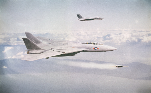 Two F14 Tomcat fighter jets engaged in a dogfight with unseen opponents. One of the Tomcats is firing a missile.