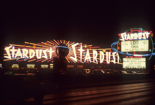 Las Vegas, Nevada- 1966: A vintage 1966's negative film scan of the Stardust hotel and casino sign in Las Vegas, Nevada with an advertisement for the Lido de Paris show and vintage 1950s cars parked in front.