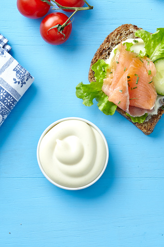 Mayonnaise and sandwich with smoked salmon, cucumber and lettuce, on a blue wooden table, top view with a free space for copy