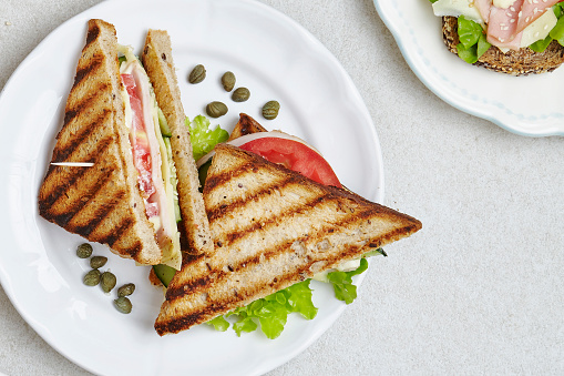 Tasty club sandwich on a plate, close up, served on a white marble kitchen or restaurant table, top view with a free space for copy
