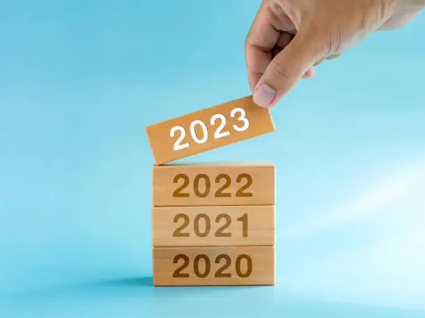 Photo of 2023 Happy New year background. 2023 calendar numbers on wooden cube blocks stacked, building by hand isolated on blue background. Business planning, trends, goal, success, and vision concepts.