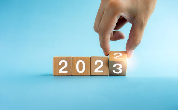 The calendar year 2022 changed to 2023, success concept. Wooden cube blocks turning by hand for the transition from 2022 to 2023, preparation for merry Christmas and happy new year on blue background. The calendar year 2022 changed to 2023, success concept. Wooden cube blocks turning by hand for the transition from 2022 to 2023, preparation for merry Christmas and happy new year on blue background. 2023 2022 stock pictures, royalty-free photos & images