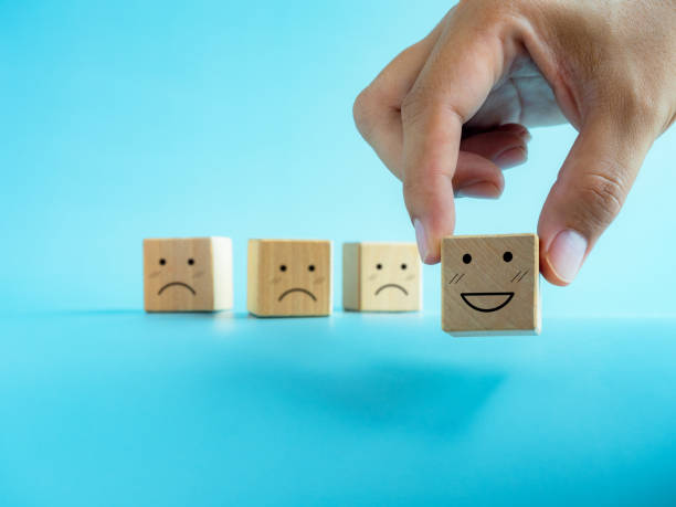 istock Rating, customer service evaluation, feedback, and satisfaction survey concepts. Hand chosen one from others choice, holding happy smile emoticon face on the wooden cube block on blue background. 1420753749