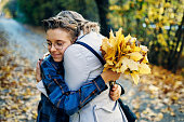Teenage boy with with bouquet of autumn leaves is hugging his mother.