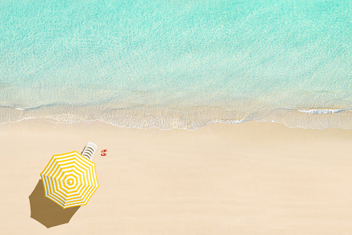 Aerial view of sunbed, lounge, flip flops, yellow umbrella on sandy beach. Summer and travel concept. Blue, turquoise transparent water surface of ocean, sea, lagoon. Aerial, drone view