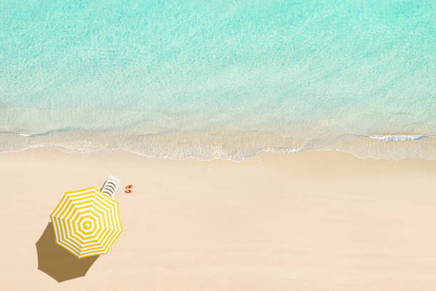 Aerial view of sunbed, lounge, flip flops, yellow umbrella on sandy beach. Summer and travel concept. Blue, turquoise transparent water surface of ocean, sea, lagoon. Aerial, drone view stock photo