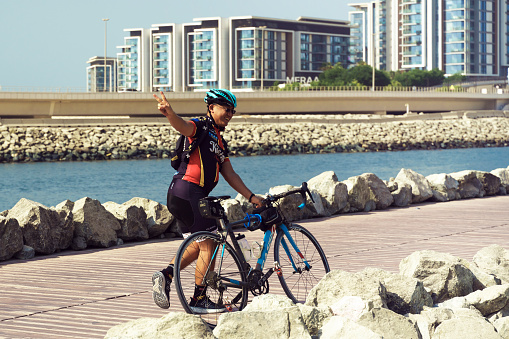 Dubai, UAE November 19, 2021: Happy cyclist on Dubai street, Dubai Marina, road leading to Ain Dubai Ferris Wheel, United Arab Emirates