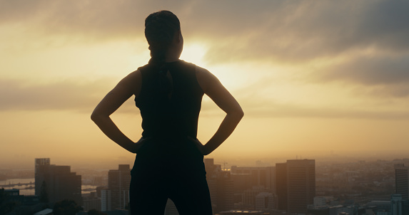 Fitness goals, exercise and sunset over urban city background while out for a run or cardio workout. Strong, powerful and proud woman runner or athlete watching view while taking a break from running