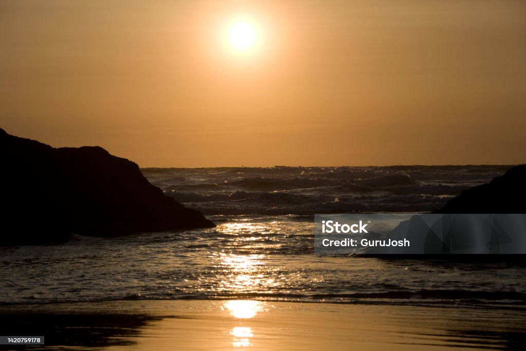Sun setting with a golden glow and reflections of light of the sea Sunset at Perranporth Beach, Cornwall Beach Stock Photo