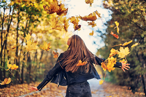 Portrait of a teenage girl throwing the fall leaves in the air. The smiling girl is spinning among the falling leaves.\nSunny fall day.\nCanon R5