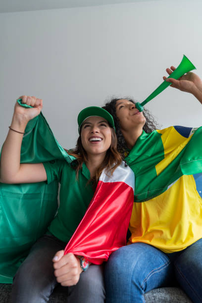 istock Pair of friends from different countries dressed to watch their match between both teams on television 1420768322