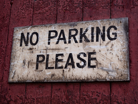 An old and considerably weathered sign reading “No Parking Please” attached to a wooden gate.