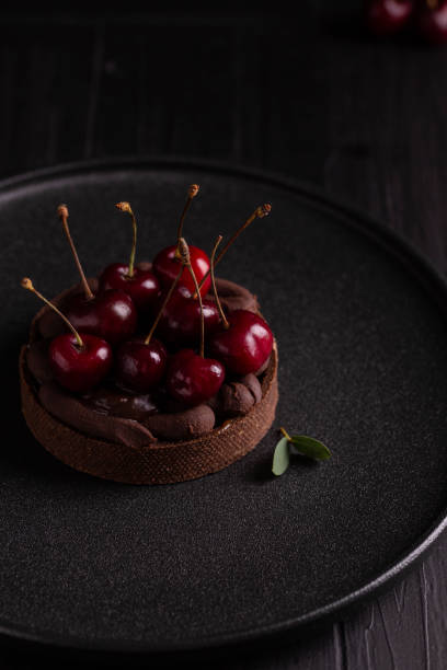 istock Cake with cherry and chocolate cream on a black plate 1420770191