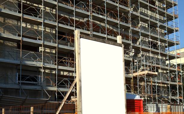 istock Blank information board outside the construction site with a new concrete building among scaffolding 1420772930