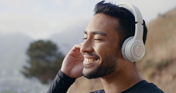 Man on walk in nature while listening to music on the radio or podcast with wireless headphones. Fit, active and healthy runner on a wellness, sports and mental health run for fitness and exercise.