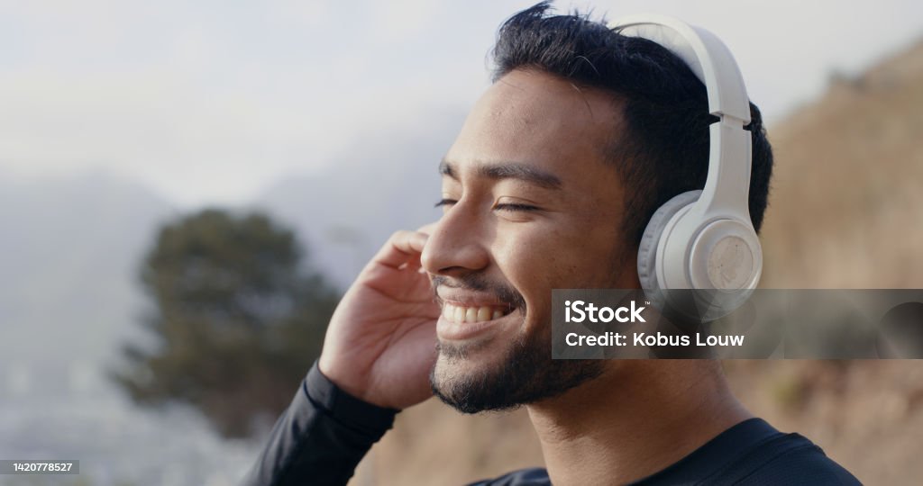 Man on walk in nature while listening to music on the radio or podcast with wireless headphones. Fit, active and healthy runner on a wellness, sports and mental health run for fitness and exercise. Music Streaming Service Stock Photo