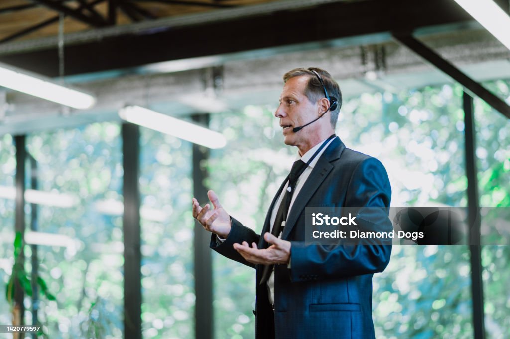 Cinematic image of a conference meeting. Cinematic image of a conference meeting. Business people sitting in a room listening to the motivator coach. Representation of a Self growth and improvement special event Public Speaker Stock Photo