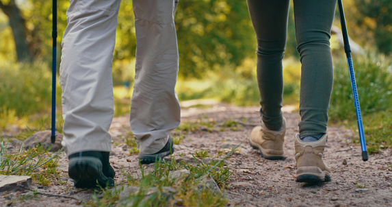 Hikers hiking or walking on a trail or dirt terrain in a forest or in the woods having fun in nature. Feet of people trekking outdoors on a trip or on holiday enjoying the environment