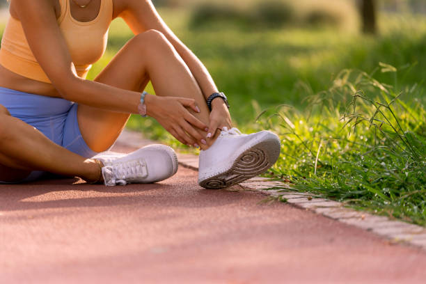 close up shot of a 20s woman on a running track with yellow tops and blue tights holding her ankle in pain - twisted ankle imagens e fotografias de stock