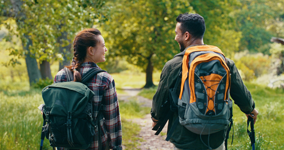Couple hiking in nature for freedom, travel and adventure from the back and walking together. Happy, smile and relax young people laughing, bonding and enjoying peaceful, calm and green outdoor date