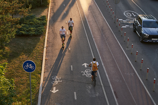 Top aerial view of cyclist and two mans are riding on kick scooters on cycling road. Concept of active lifestyle.