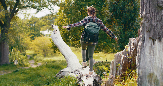 Adventure, hiking and nature travel with young woman exploring and having fun in a forest while balance walking on fallen tree. Backpacker traveling and spending time outdoors for health and wellness