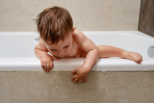 Cute little Asian 2 years old toddler baby boy child having fun sitting in bathtub playing rubber duck toy and take a shower by himself in the bathroom, baby care concept, Shallow DOF Selective focus