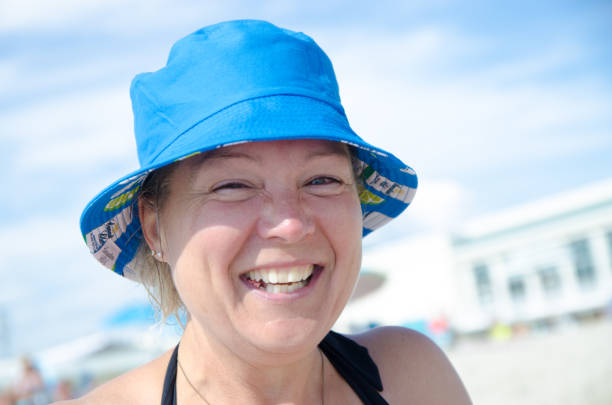 Headshot of mature woman with blue hat laughing at the beach during summer day