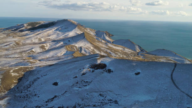 vista aérea de rochas nevadas, mar azul, no fundo do céu nublado. injeção. colinas cobertas de neve na islândia à beira-mar em um dia de inverno. - rear view winter blizzard nordic countries - fotografias e filmes do acervo