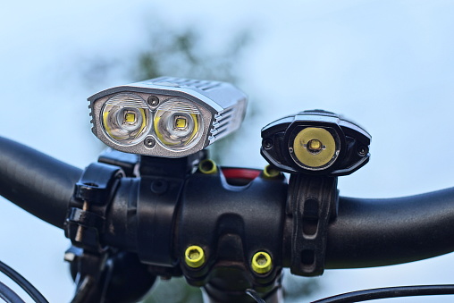 part of a black metal bicycle handlebar with two LED lights on the street