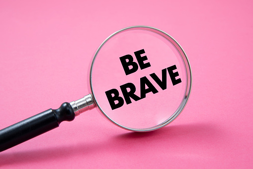 Words be brave in a magnifying glass on pink background