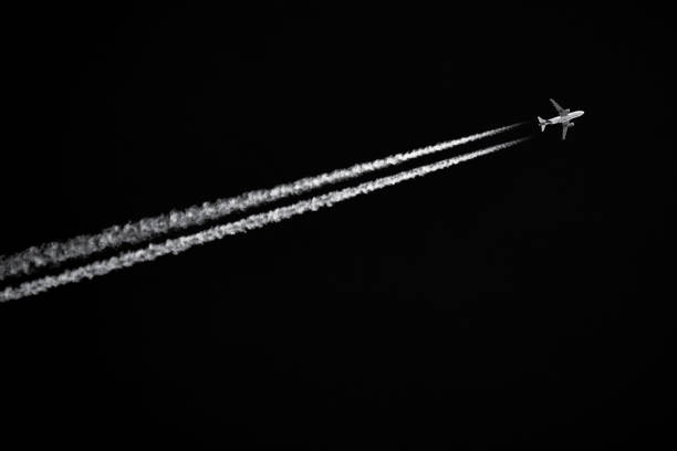 Twin-engined jetliner with contrails flying in black sky